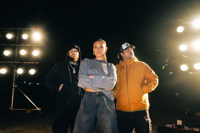 Promotional photo of Australian First Nations hip-hop group 3% posing outdoors at night under bright venue stage lighting.