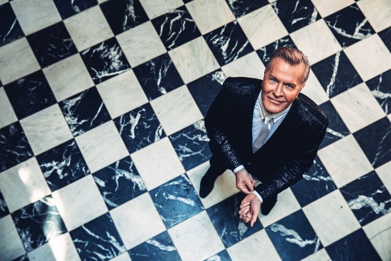 High-angle shot of Martin Fry from band ABC wearing a black suit on a black-and-white checkered marble floor looking up.