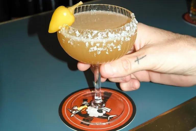 Cocktail at Bar Bar garnished with a yellow pepper and a coarse salt rim, served in a ribbed coupe glass.