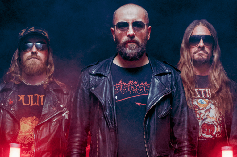 Promotional portrait of Swedish death metal band Bloodbath posing in leather jackets under moody red and blue lighting.