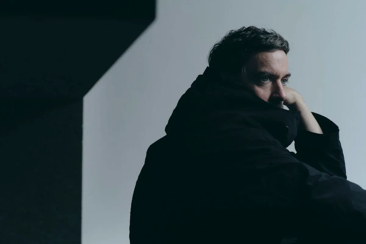 Electronic musician Bonobo (Simon Green) in a moody press portrait wearing a high-collared black jacket, photo credit Ryohei Ambo.