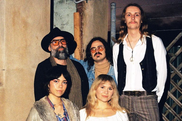 Five members of the band Caressa posing together outdoors in retro-inspired 1970s fashion.