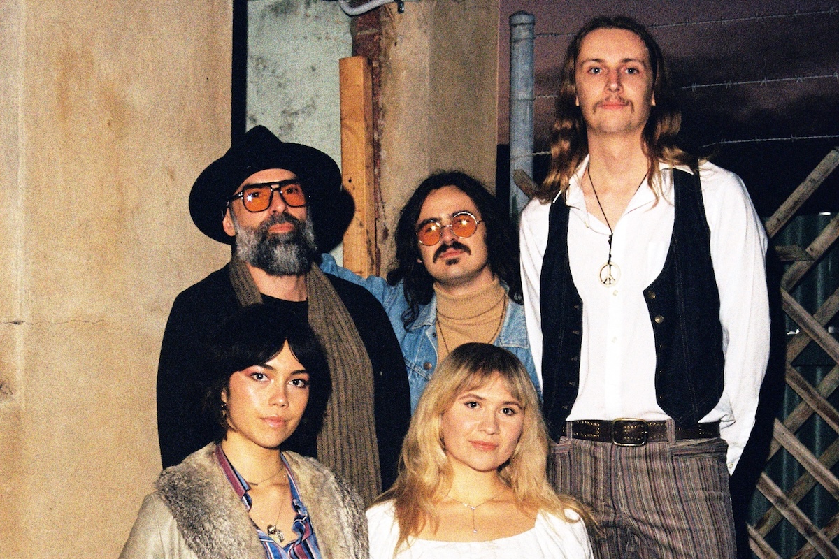 Five members of the band Caressa posing together outdoors in retro-inspired 1970s fashion.