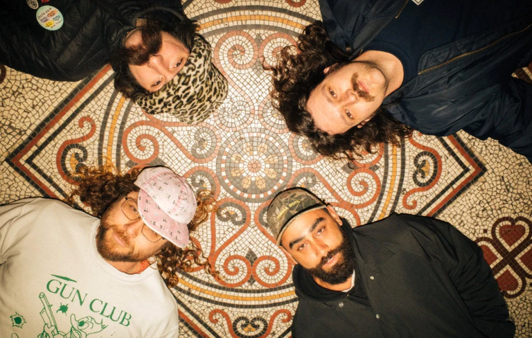 Members of Australian punk rock band COFFIN lying in a circle looking up at the camera while arranged on a detailed geometric mosaic tile floor. (142 characters)
