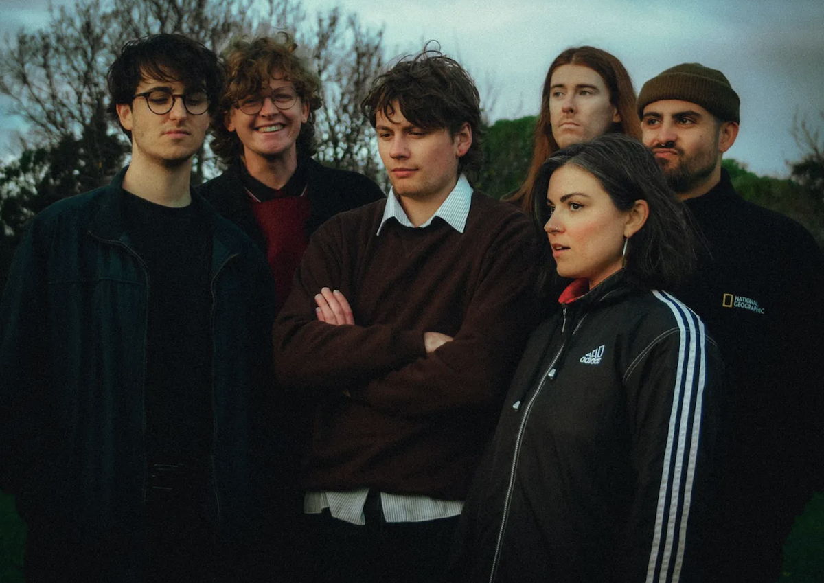 Adelaide post-punk band Coldwave posing outdoors at dusk for a press photo shoot, featuring six members in casual jackets, sweaters, and beanies.