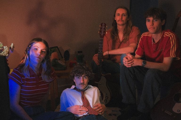 Indie band Destinezia posing together in a dimly lit, vintage room illuminated by moody blue and warm ambient lighting.