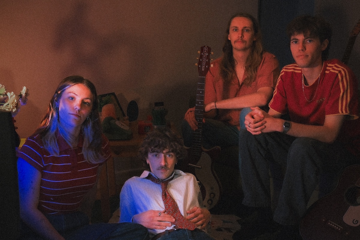 Indie band Destinezia posing together in a dimly lit, vintage room illuminated by moody blue and warm ambient lighting.