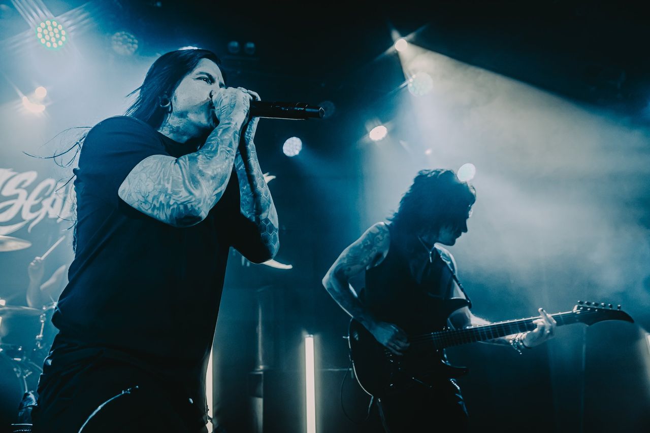 Escape the Fate vocalist Craig Mabbitt singing into microphone alongside guitarist performing live under cool blue stage lights.