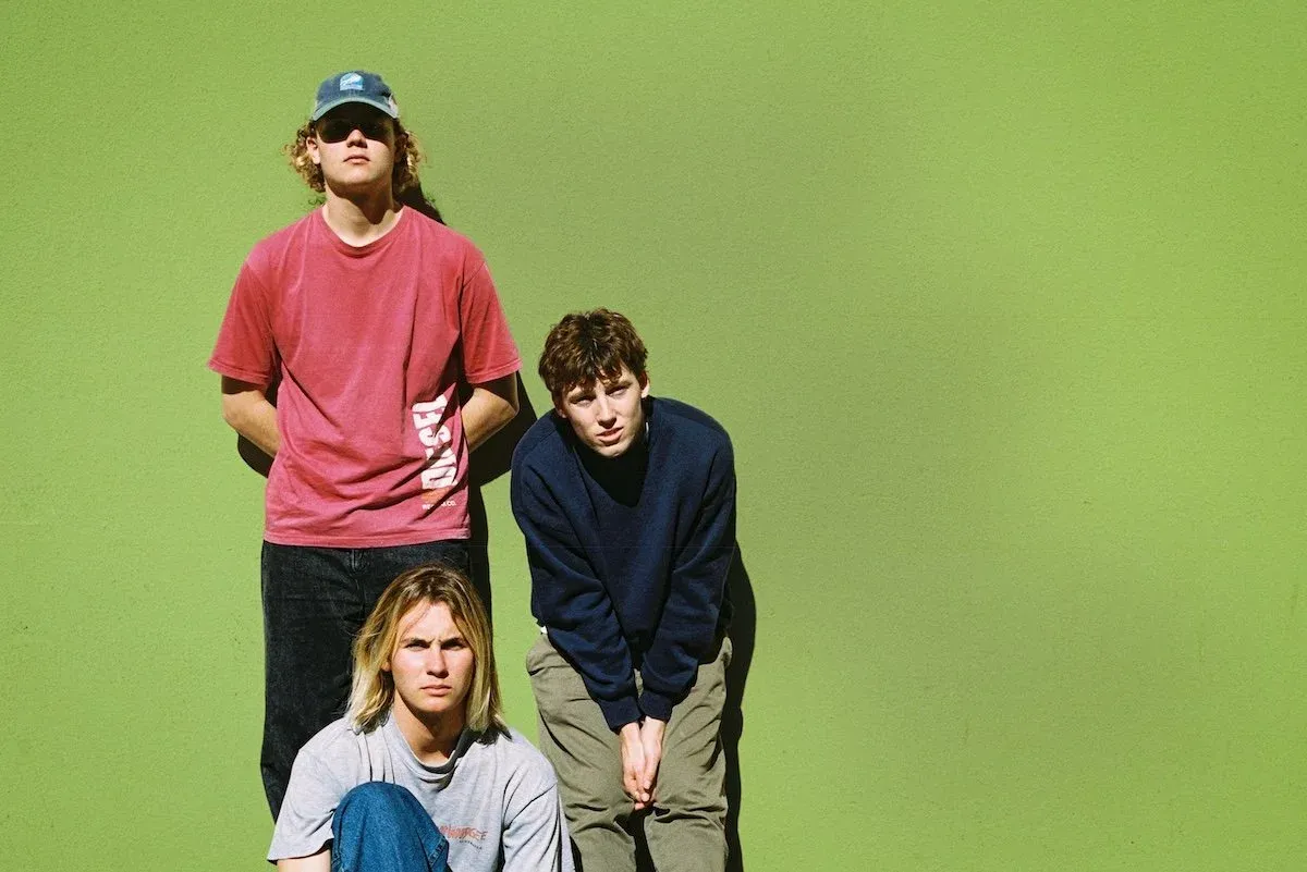Indie rock band Fool Nelson posing against a bright green wall in casual streetwear including t-shirts, a cap, and a dark blue sweater.