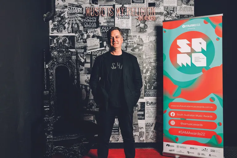 Music industry professional Joy Hay standing between an ornate dark throne and a South Australian Music Awards banner.
