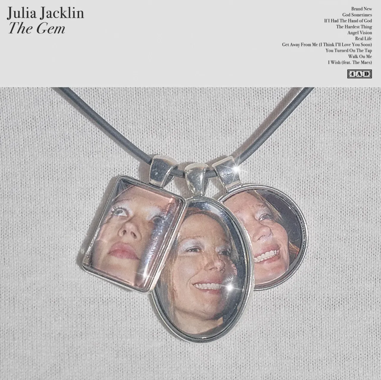 Album artwork for Julia Jacklin's "The Gem," showing a black cord necklace with three silver pendants featuring her face over a white textured background.