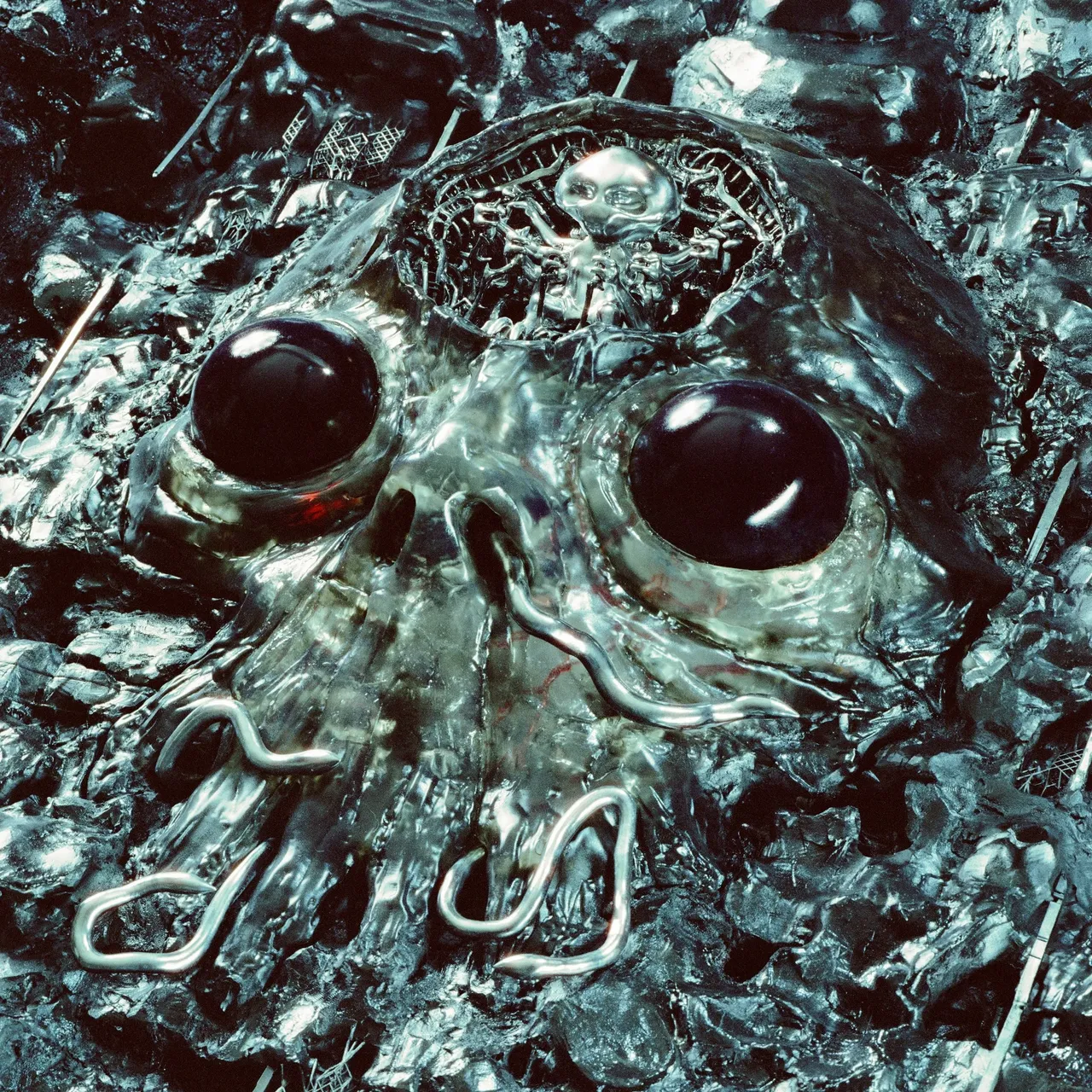 King Gizzard and the Lizard Wizard metallic alien skull album artwork, featuring large glossy dark eyes and a small grey alien pilot inside.