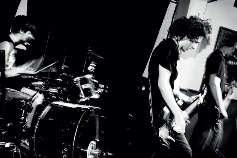 Black and white photo of rock band Ledfly performing live on stage, featuring a drummer and two guitarists captured in high-contrast motion.