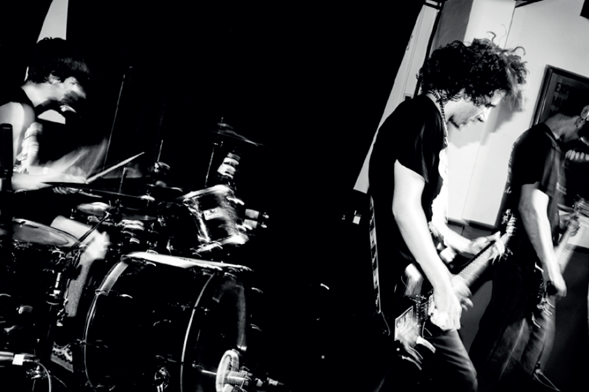 Black and white photo of rock band Ledfly performing live on stage, featuring a drummer and two guitarists captured in high-contrast motion.
