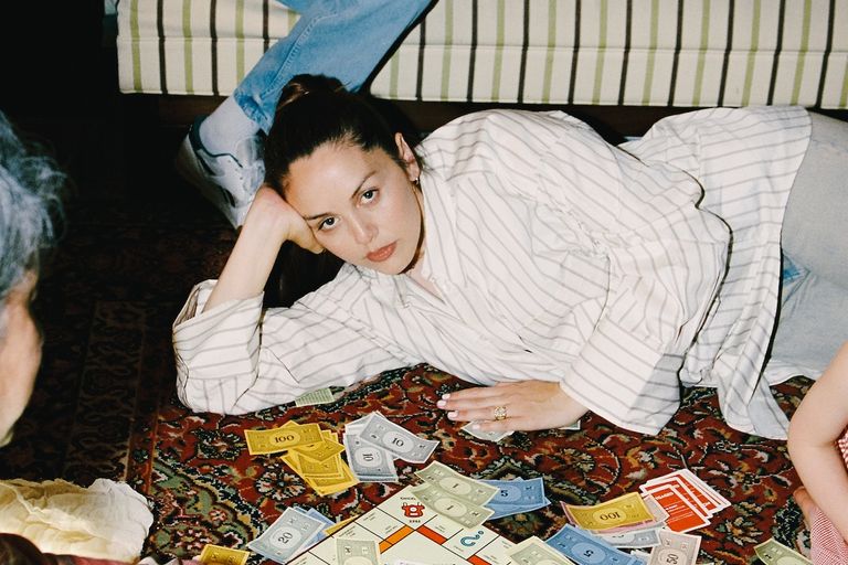 Producer Logic1000 lying on a patterned rug playing a Monopoly board game, resting her head on her hand.
