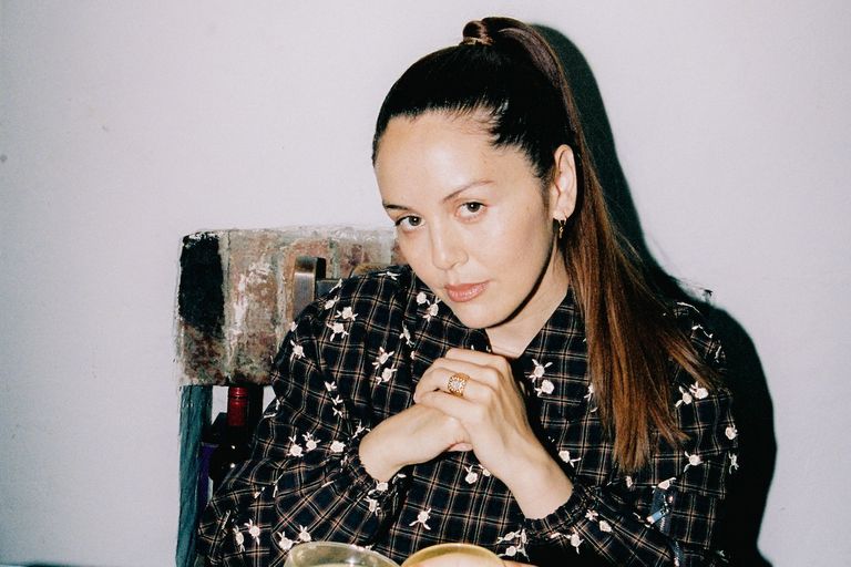 Electronic producer Logic1000, Samantha Poulter, with a high ponytail in a dark plaid shirt resting her hands together in a promo portrait.