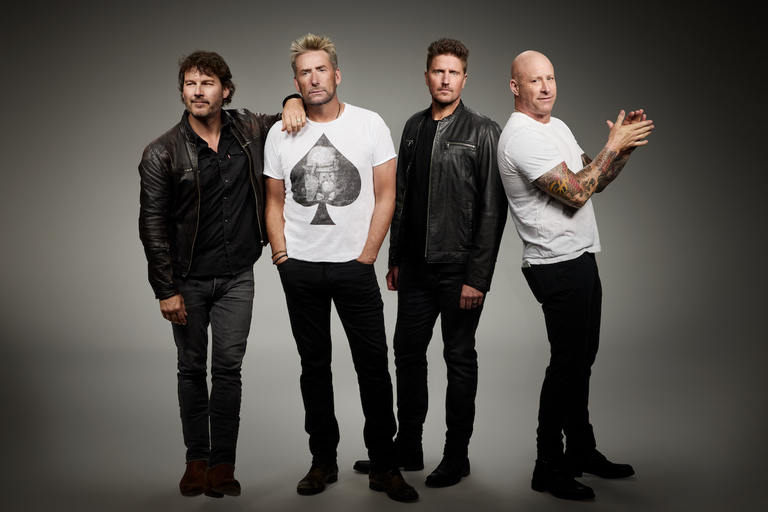 Canadian rock band Nickelback members posing together in studio attire against a neutral grey background