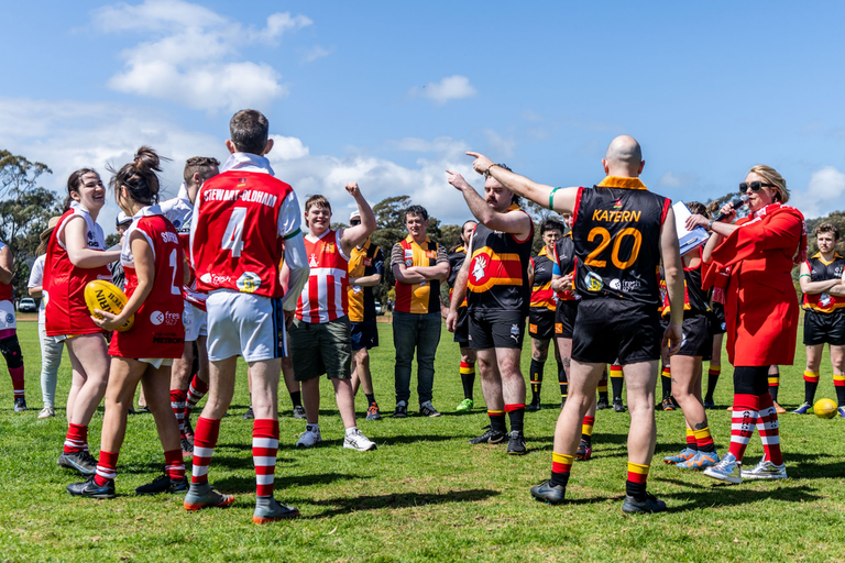 Australian rules football players gathered on a sunny field during the charity event Reclink Community Cup.