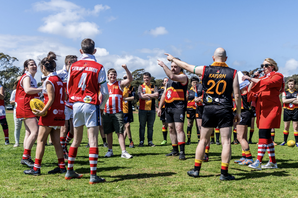 Australian rules football players gathered on a sunny field during the charity event Reclink Community Cup.
