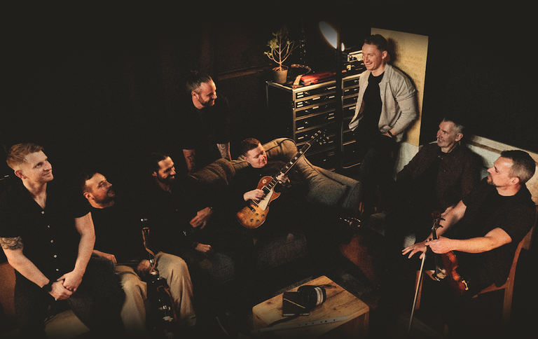Scottish Celtic rock band Skerryvore posing together in a moody studio setting with instruments including a guitar and fiddle