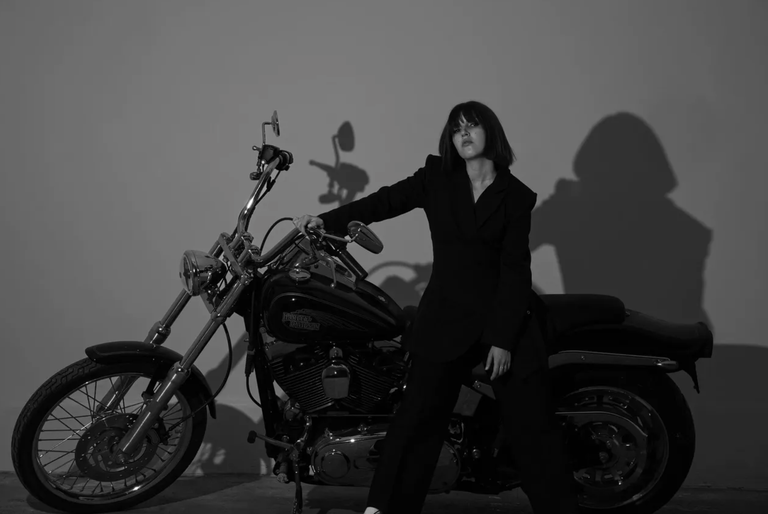 Australian pop artist Stellie posing in a black suit alongside a Harley-Davidson motorcycle in a monochrome press photo.