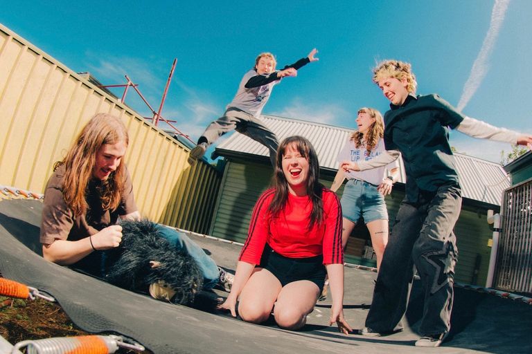 Indie band Stormy-Lou laughing and jumping on a trampoline outdoors under a clear blue sky, capturing a playful, energetic moment.