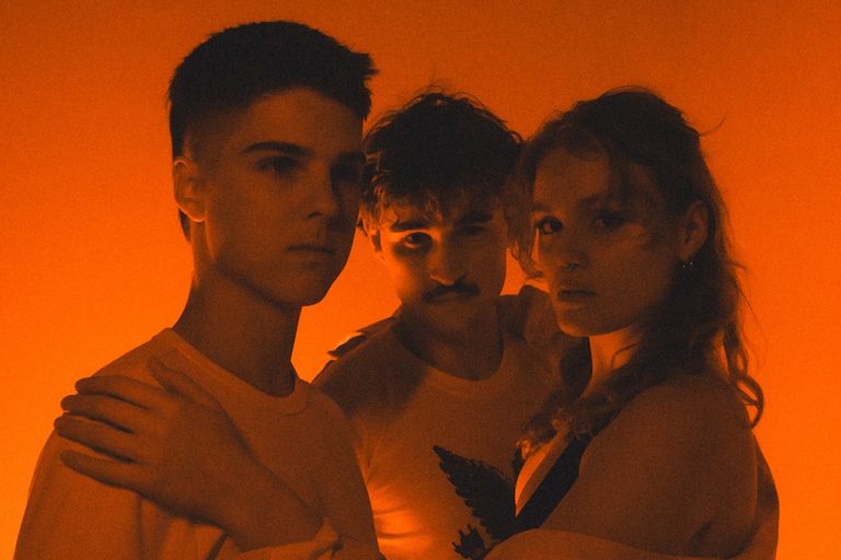 Warm orange-lit promotional portrait of three members of the music trio TONIX standing close together facing the camera.