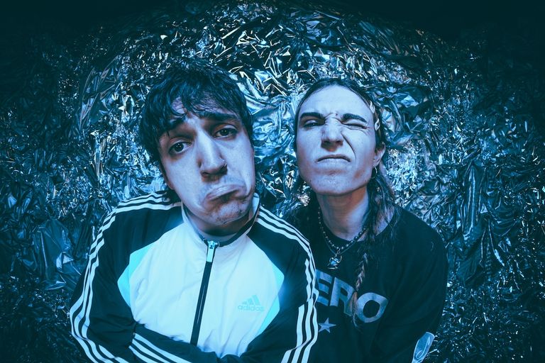 Adelaide indie duo TOWNS pulling playful expressive faces in front of a shiny metallic foil backdrop under cool blue lighting.