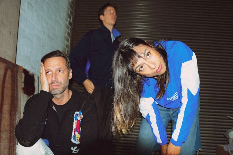 Australian alt-pop band Telenova posing near a roller shutter, with frontwoman Angeline Armstrong leaning forward in a blue jacket.
