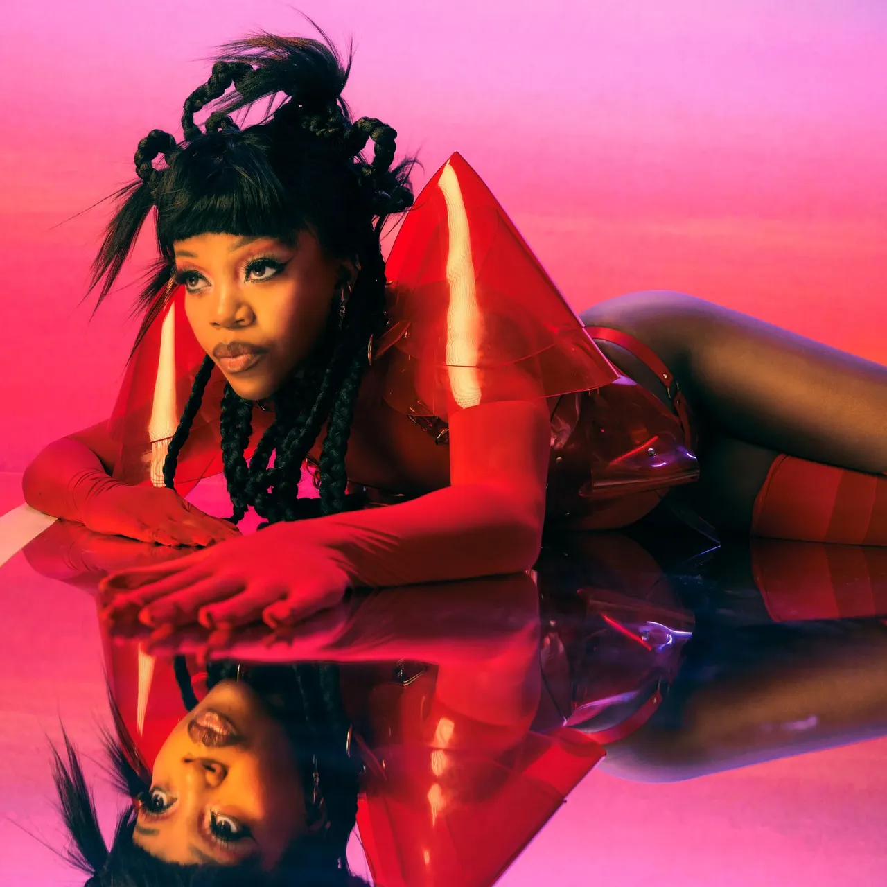 Tkay Maidza Romanticze album artwork featuring the singer reclining on a pink reflective surface in a red vinyl outfit with dramatic shoulder pieces.