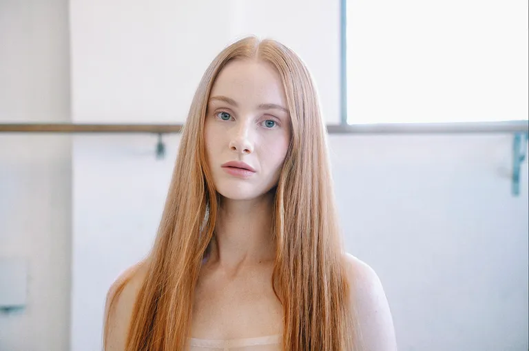 Australian singer-songwriter Vera Blue posing for a close-up portrait with long straight strawberry blonde hair against a bright background.