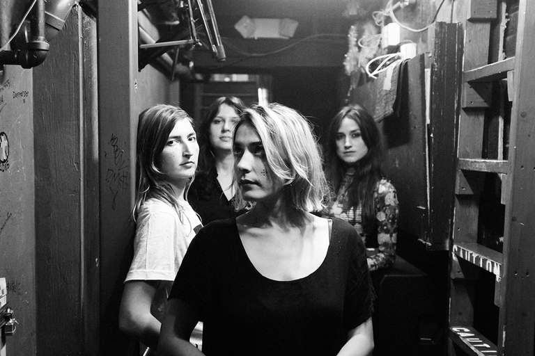 Black and white portrait of indie rock band Warpaint posing in a narrow hallway backstage.