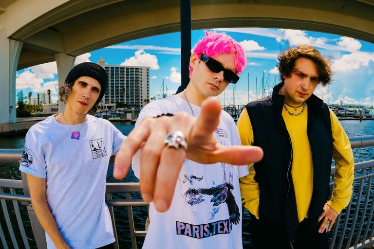 Alternative rock band Waterparks posing outdoors near a waterfront with a bridge in the background.
