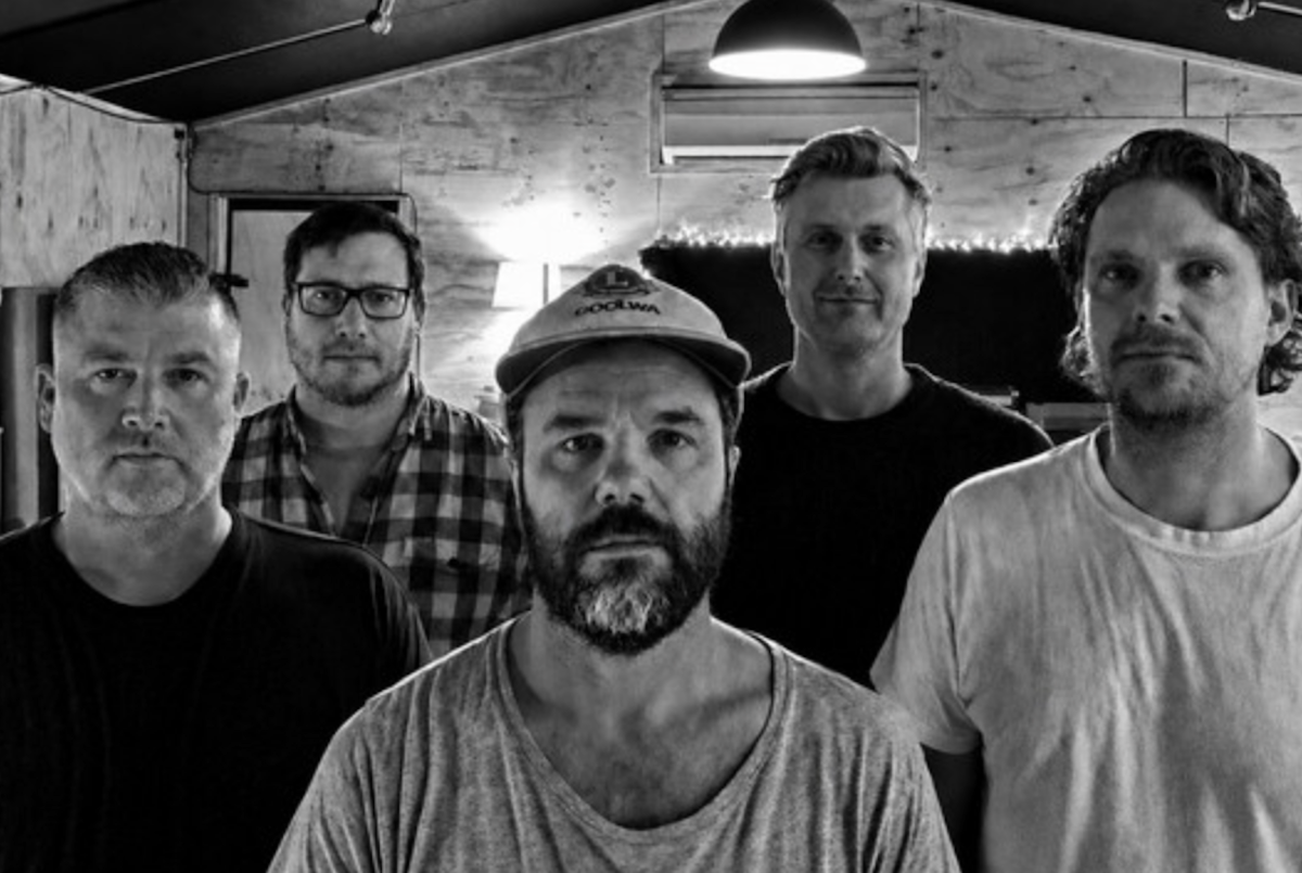 Black and white portrait of five members of indie band ...andtheworld inside a music rehearsal studio space.
