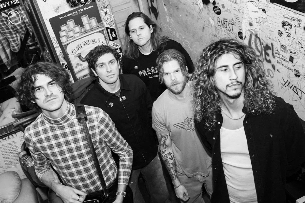 Black and white photo of rock band Culture Wars standing in a graffiti-covered hallway, with one member holding an electric guitar.