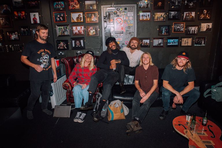 Australian psychedelic rock band Ocean Alley smiling and relaxing backstage in a green room filled with framed wall photos.
